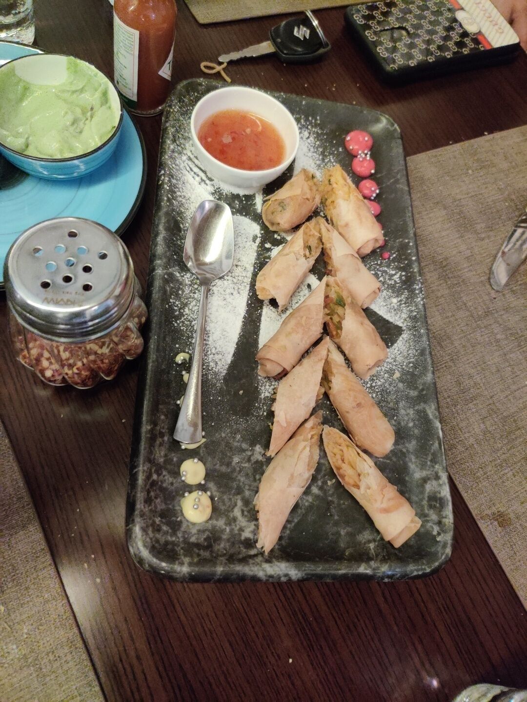 Una mesa de comedor con un plato de comida, un recipiente de salsa y condimentos.