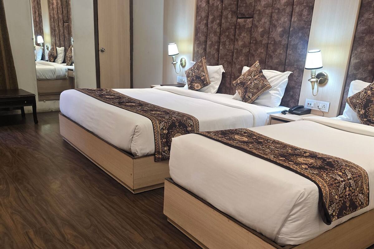 A hotel room with two beds, wooden flooring, and a large mirror.