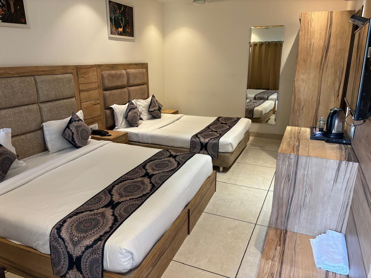Une chambre d’hôtel avec deux lits, une tête de lit en bois, une table de chevet avec une lampe et un miroir.