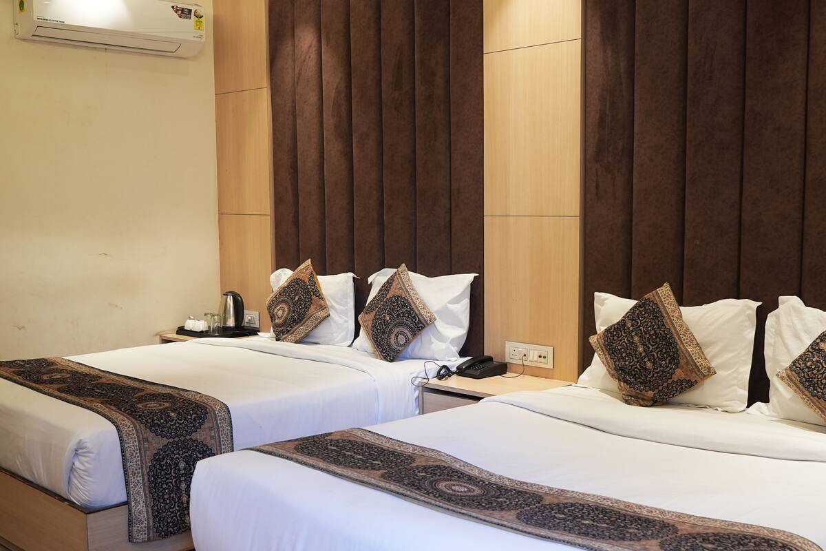 A hotel room with two beds, a wooden headboard, a bedside table with a phone, and a wall-mounted air conditioner.