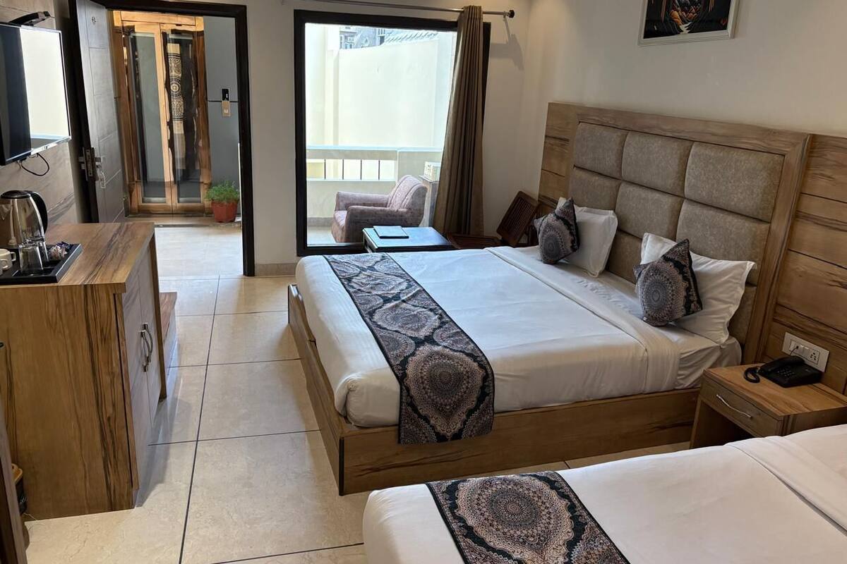 A hotel room with a large bed, a bedside table, a desk with a chair, and a view of the outside balcony.