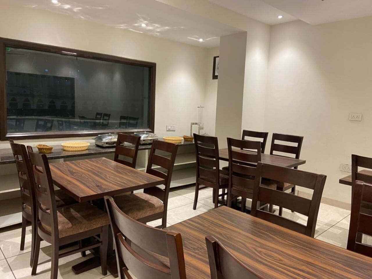 Un comedor con mesas y sillas de madera, un amplio ventanal con vistas, y una cocina con electrodomésticos y un fregadero.