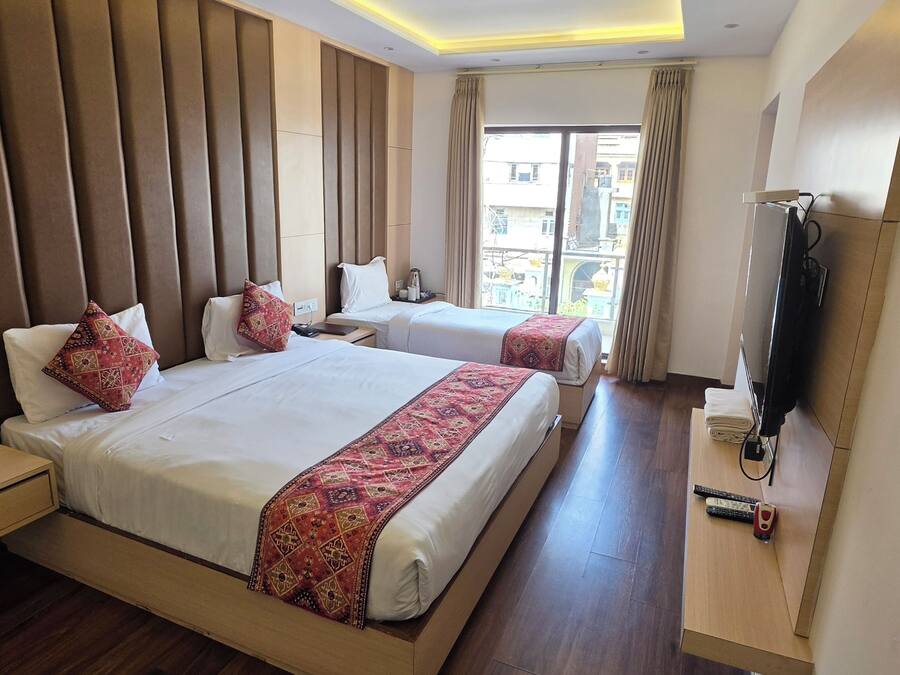 A hotel room with two beds, a television, and a window with curtains.