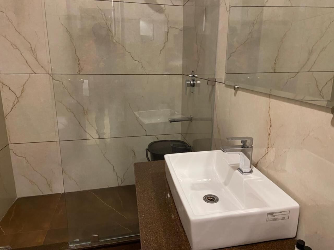 Ein Badezimmer mit einem weißen Waschbecken, einer Duschkabine aus Glas und einer Wand mit Marmorplatten.
