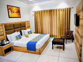 Habitación de hotel con cama de madera, mesita de noche, una silla, televisor y un amplio ventanal con cortinas.