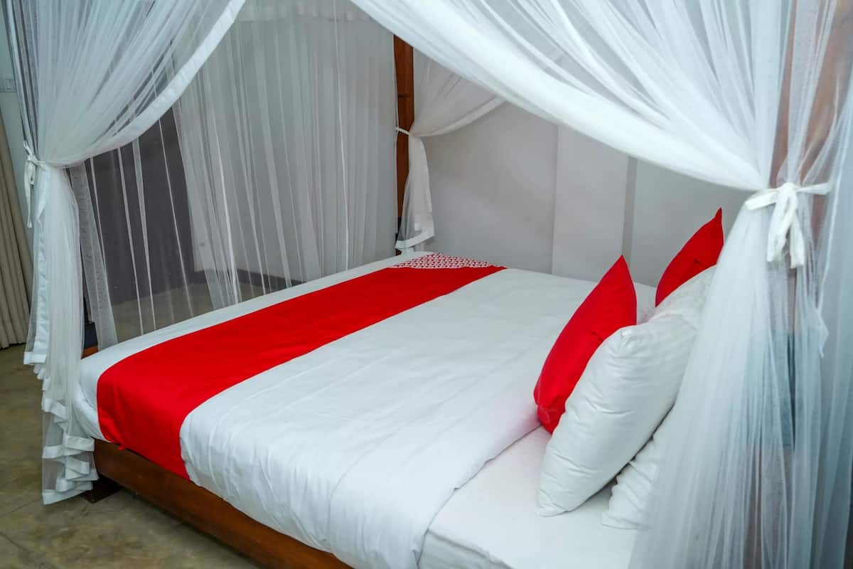 Una cama con dosel blanco y detalles rojos, estructura de madera y colcha roja y blanca.