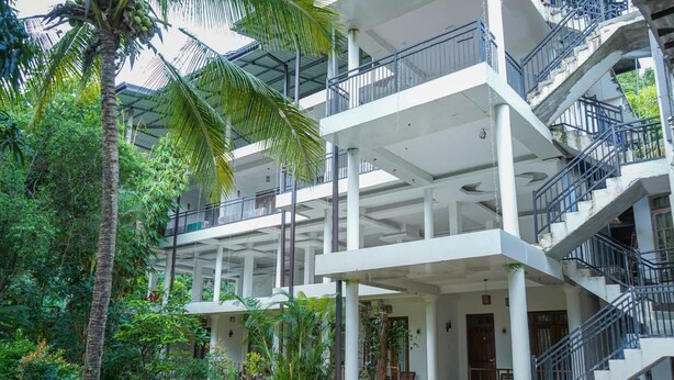 Un edificio de varios pisos con balcones y escaleras, rodeado de abundante vegetación.