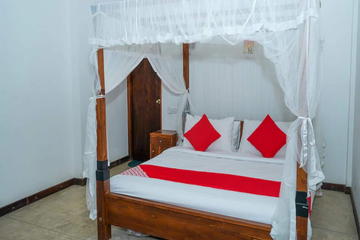Una cama con dosel, con dosel blanco, almohadas rojas y cabecera de madera.
