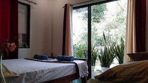 Ein Schlafzimmer mit Bett, Kissen, einer Vase mit Blumen und Blick auf Grün hinter dem Fenster.
