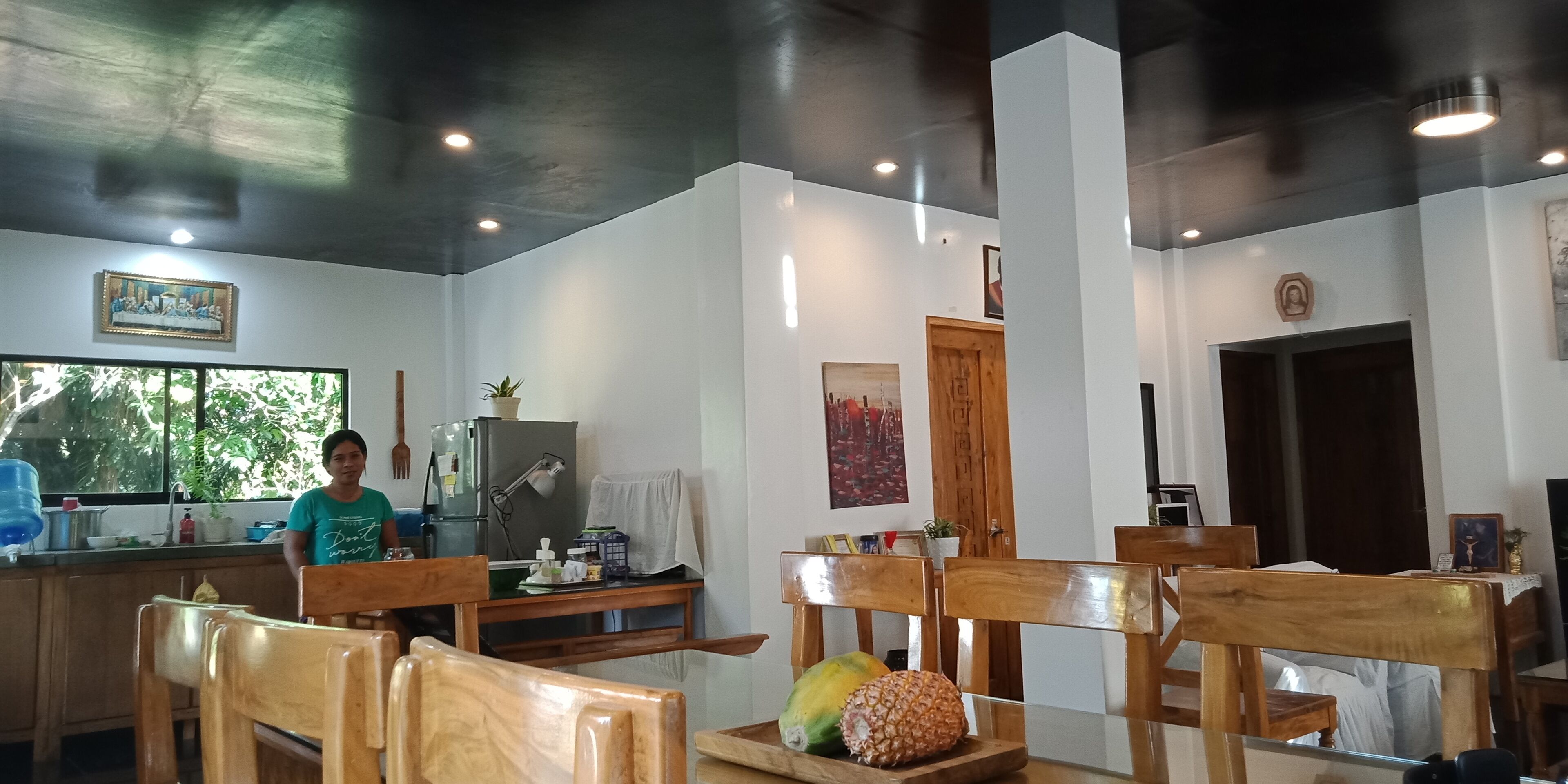 A dining area with wooden chairs and a table, a refrigerator, a sink, and a window with a view of trees.
