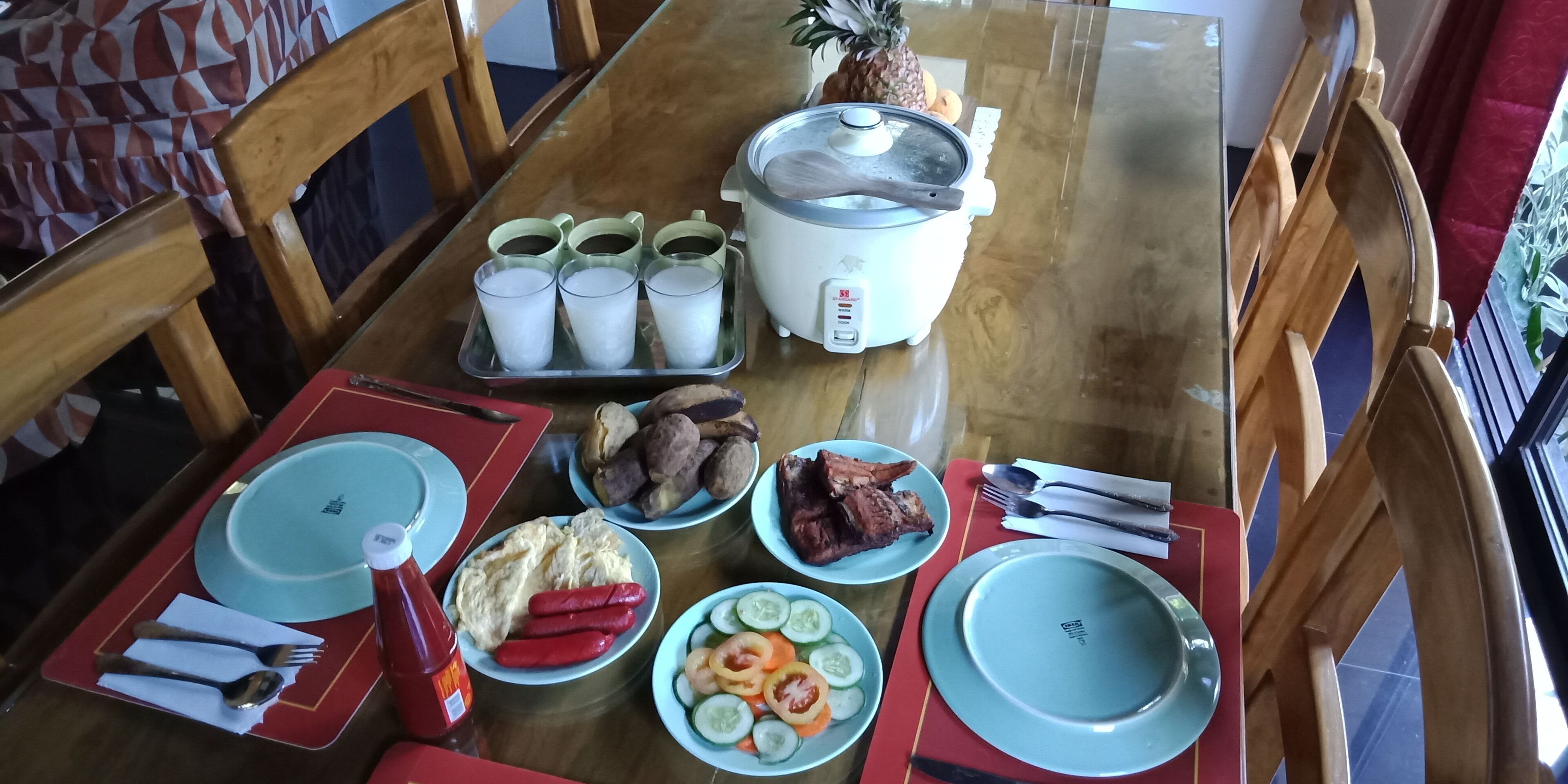 Una mesa de comedor dispuesta con platos, cubiertos y diversos platos, incluyendo huevos, salchichas y verduras.