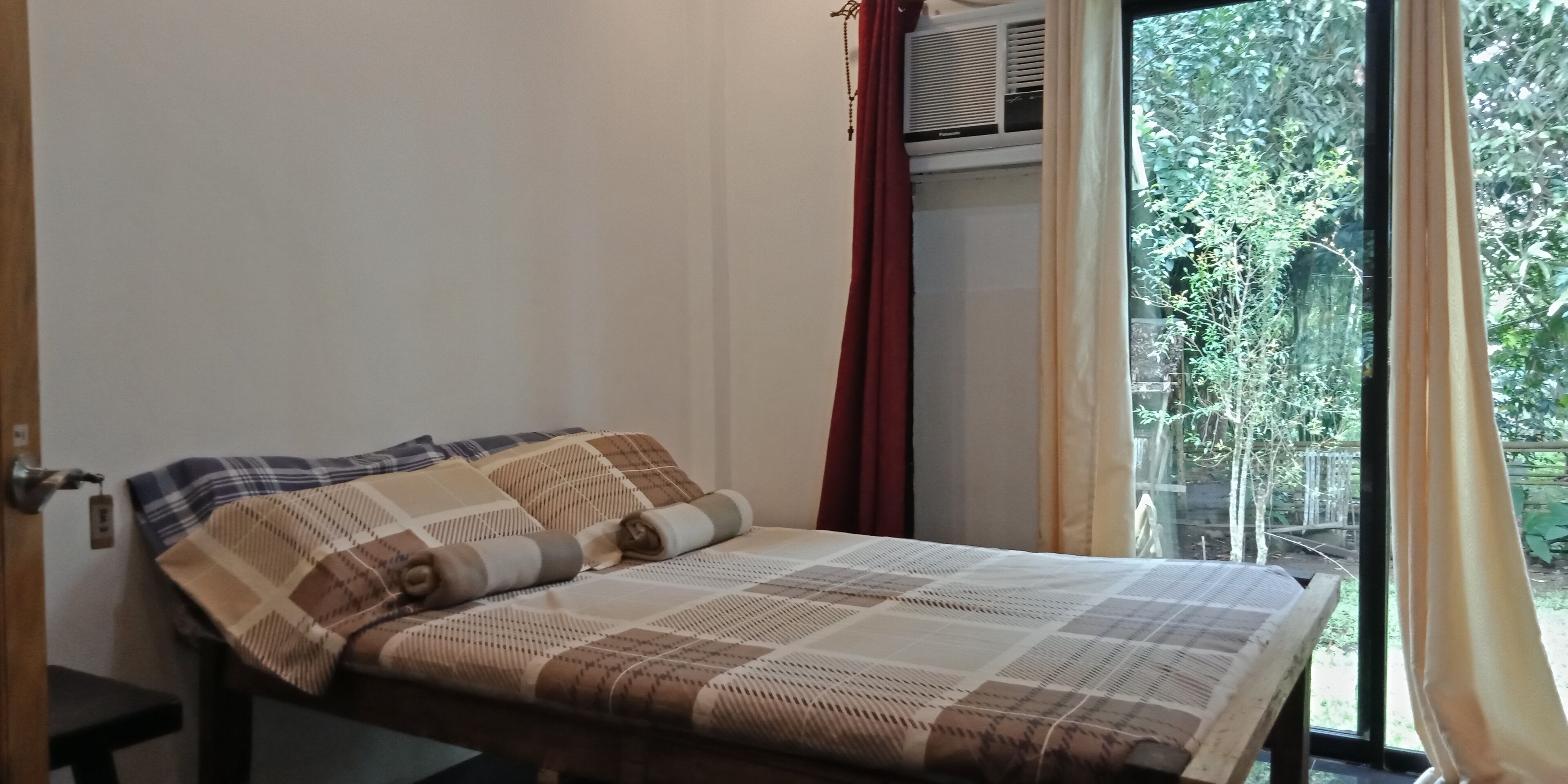 Un letto con copriletto a quadri, una finestra con tende e un condizionatore d'aria.