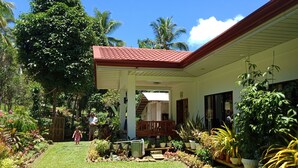 Ein Haus mit rotem Dach, einer Veranda und einem Garten mit verschiedenen Pflanzen und einem Rasen.