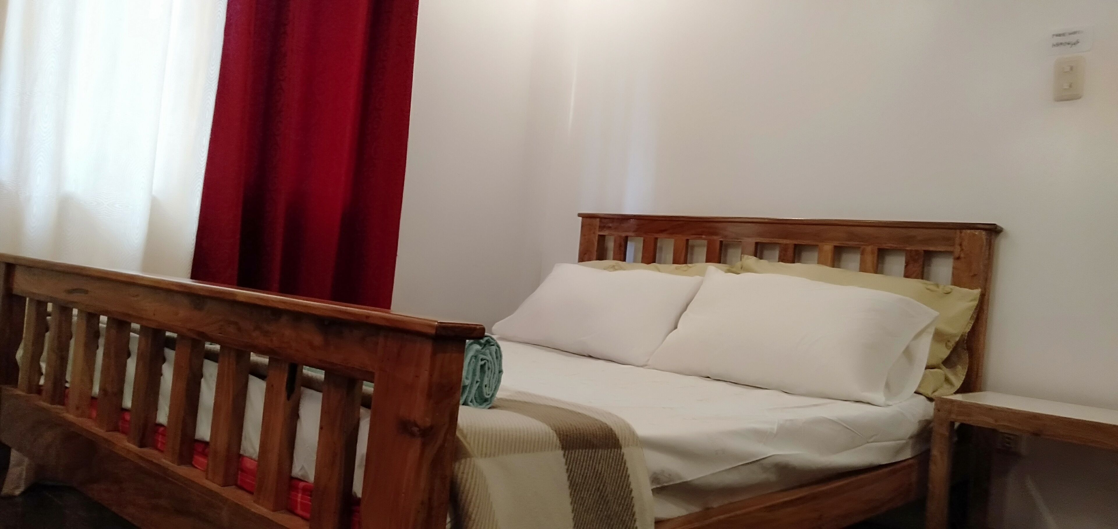 Una cama de madera con ropa de cama blanca, un cabecero de madera y una cortina roja.