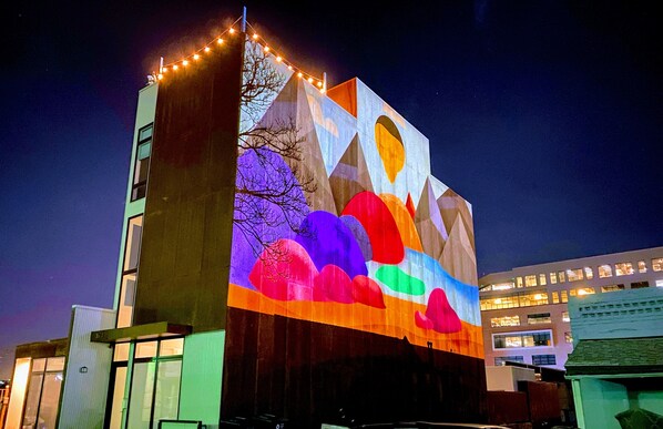 A building with a large illuminated mural on its side, featuring geometric shapes and abstract designs.