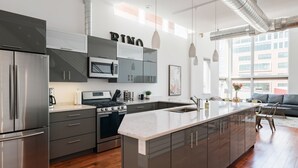 Una cucina moderna con elettrodomestici in acciaio inossidabile, un'isola centrale e una zona pranzo con divano e tavolo.
