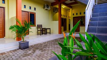 A covered outdoor area with a tiled floor, a potted plant, a wooden chair, and a staircase.
