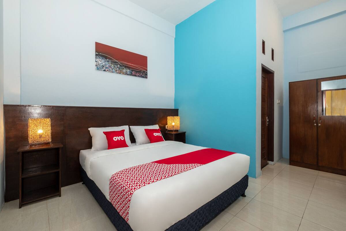 A neatly arranged bedroom with a large bed, two bedside tables with lamps, a wardrobe, and a wall-mounted artwork.