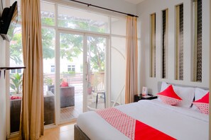 A hotel room with a bed, curtains, a nightstand, and a view of the outdoor patio. - OYO 2376 Tiara Residence Syariah (Batu)