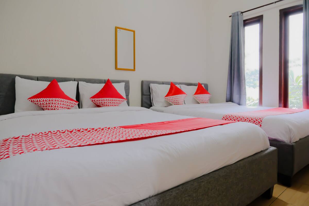 A hotel room with two beds, each with red and white bedding, grey headboards, and a large window with curtains.
