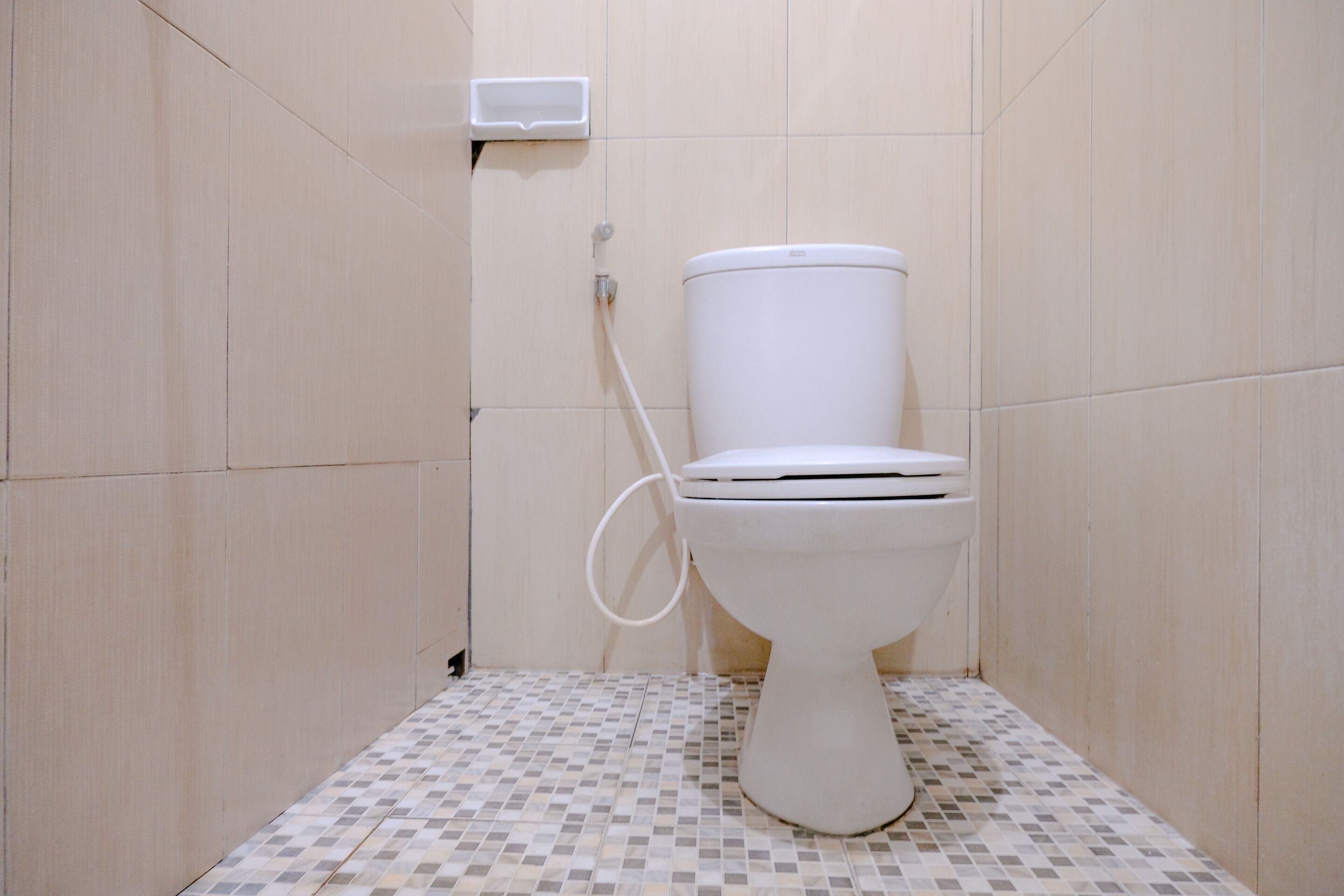 A bathroom with a toilet, a wall-mounted soap dispenser, and a tiled floor.