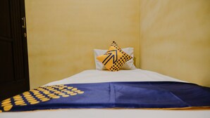 A bed with a blue and yellow patterned bedspread, a white pillow with a yellow and blue design, and a plain yellow wall. - SPOT ON 2387 Bukit Cemara Tidar Family (Malang)