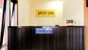 Una mesa de recepción con un cartel que dice "SPOT ON" y otro cartel debajo que dice "RESEPSIONIS PENGINAPAN TLOGOREJO 2".