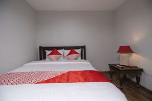 A neatly made bed with a red and white patterned bedspread, a wooden nightstand with a lamp, and two red pillows. - OYO 2438 D' Tamblingan Guesthouse (Jimbaran)