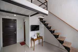 A modern interior with a staircase, a flat-screen TV mounted on the wall, and a small wooden table with a red mat. - OYO 2438 D' Tamblingan Guesthouse (Jimbaran)