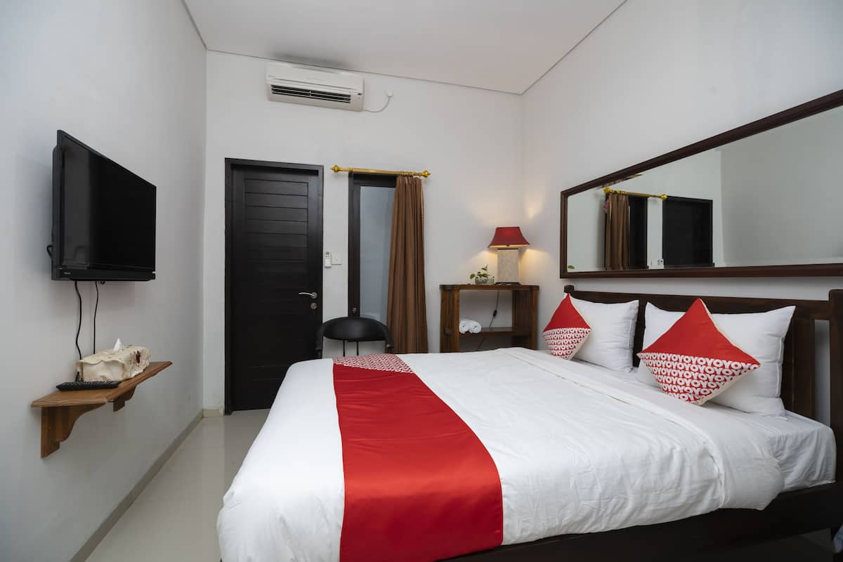 Ein Hotelzimmer mit Bett, Wandfernseher, Nachttisch mit Lampe und Spiegel über dem Bett.