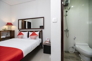 Ein Hotelzimmer mit Bett, Nachttisch mit Lampe, Spiegel, Duschbereich mit Toilette und einem kleinen Tisch mit Taschentuchbox.