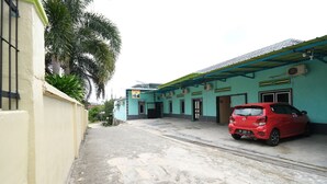 A building with a red car parked in front, a paved walkway, and a green and blue exterior. - OYO 2389 Kostel 99 (Pangkalpinang)