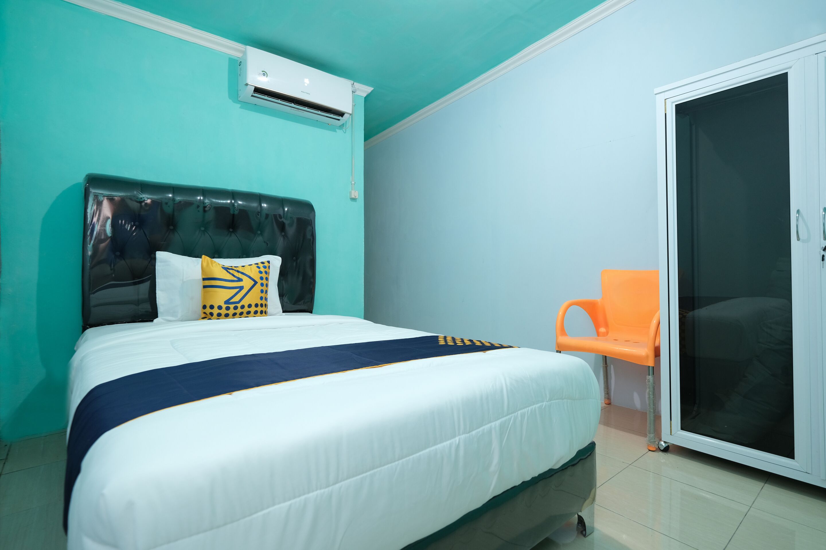 Quarto com cama, ar-condicionado, porta deslizante e uma cadeira laranja.