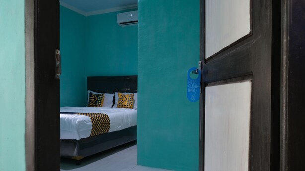 A room with teal walls, a bed with patterned bedding, and a sign indicating cleaning is needed. - OYO 2389 Kostel 99 (Pangkalpinang)