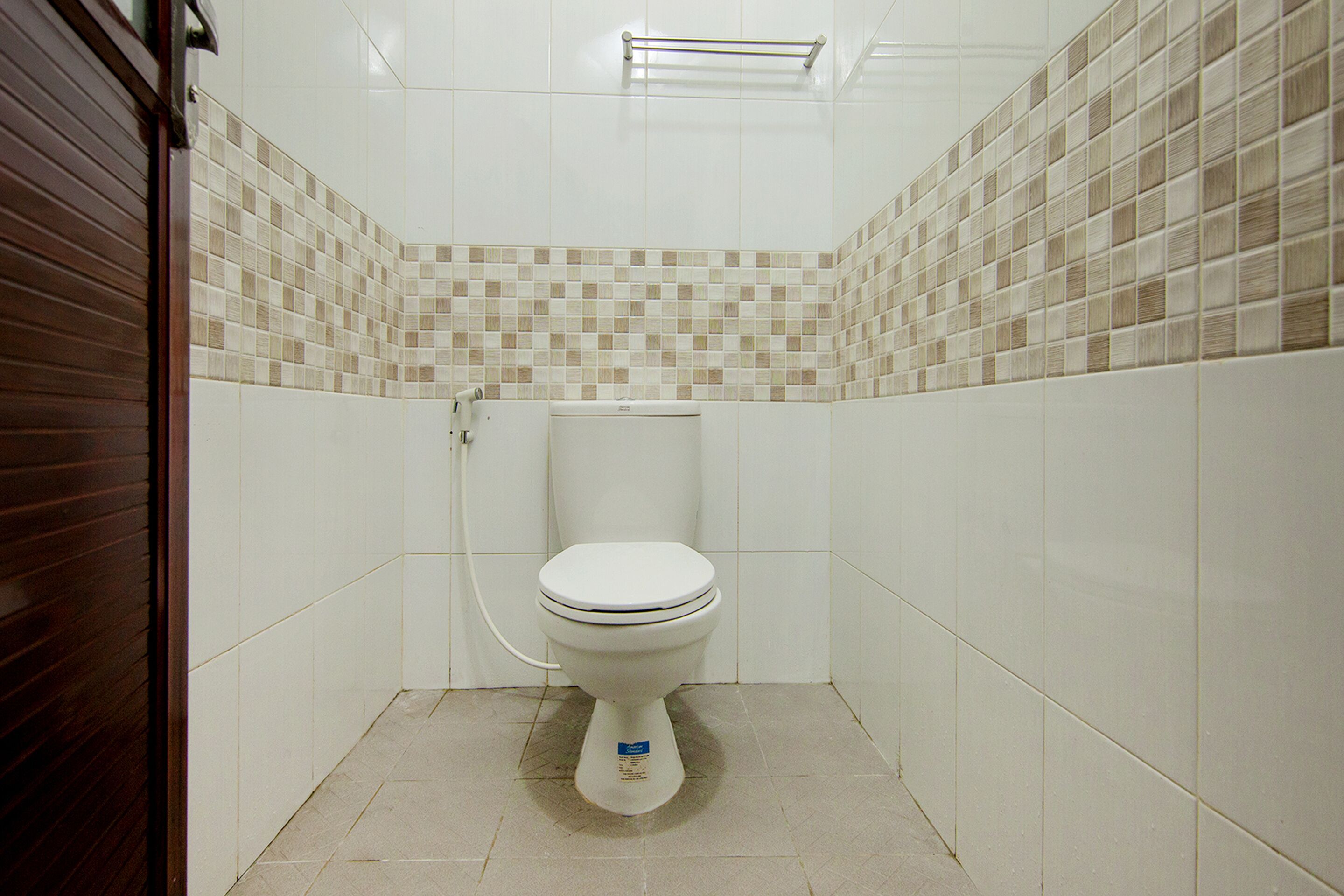 Un baño pequeño con azulejos, un inodoro, un perchero y una tubería a la vista.