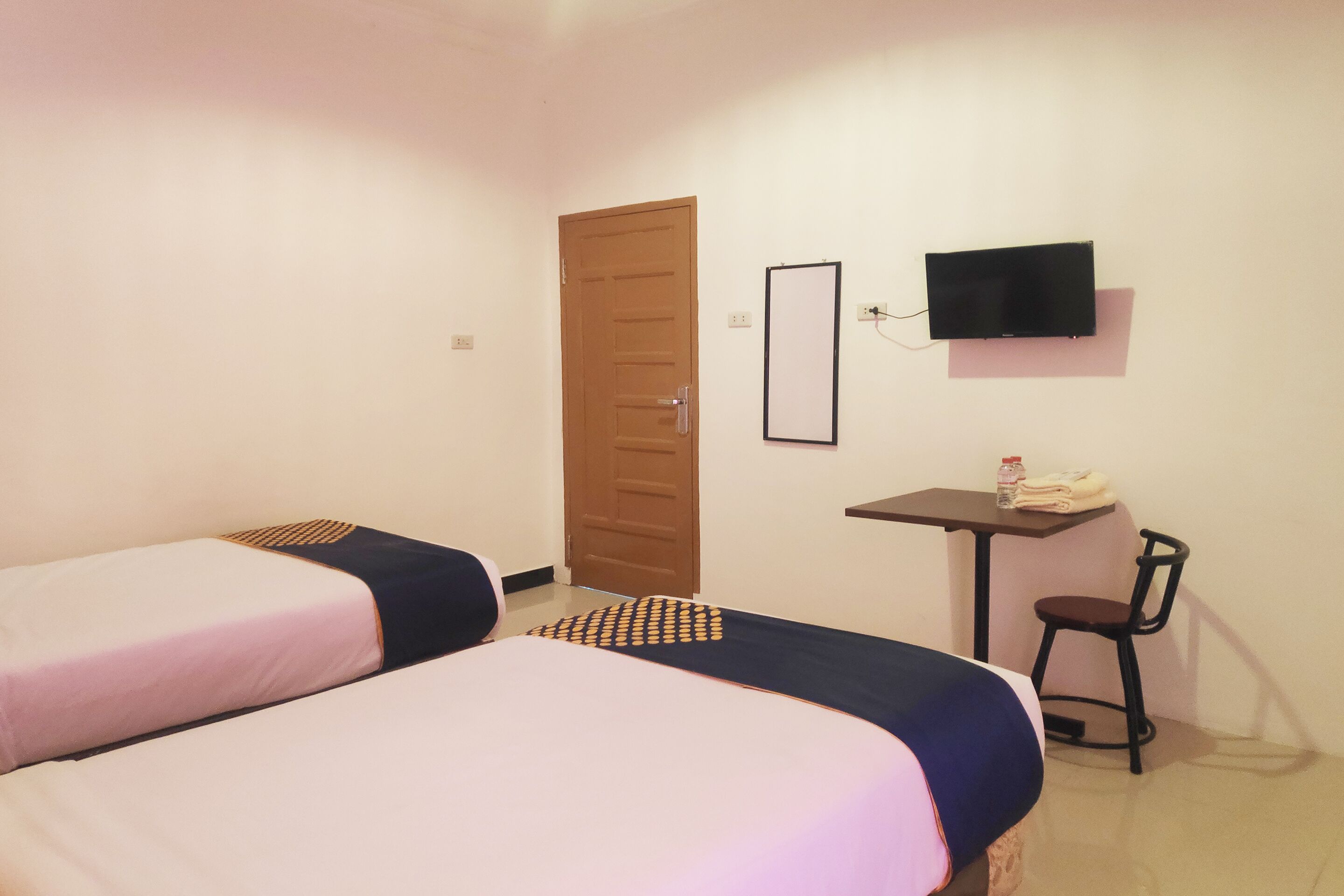 A room with two beds, a TV, a small table with a chair, and a door.