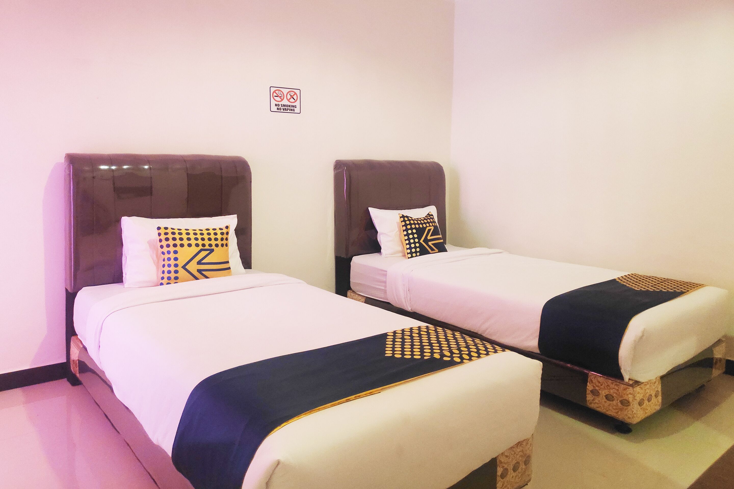 Two single beds with headboards, white bedding, and decorative pillows. A 'No Smoking' sign is visible on the wall.