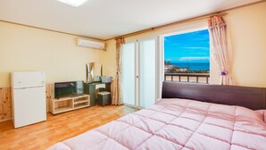 A bedroom with a bed, a TV, a small fridge, a desk, and a window with a view of the sea. - Vellise Pension (Taean)