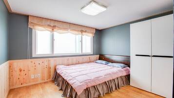 A bedroom with a wooden headboard, a bed with pink bedding, a window with curtains, and a wardrobe.