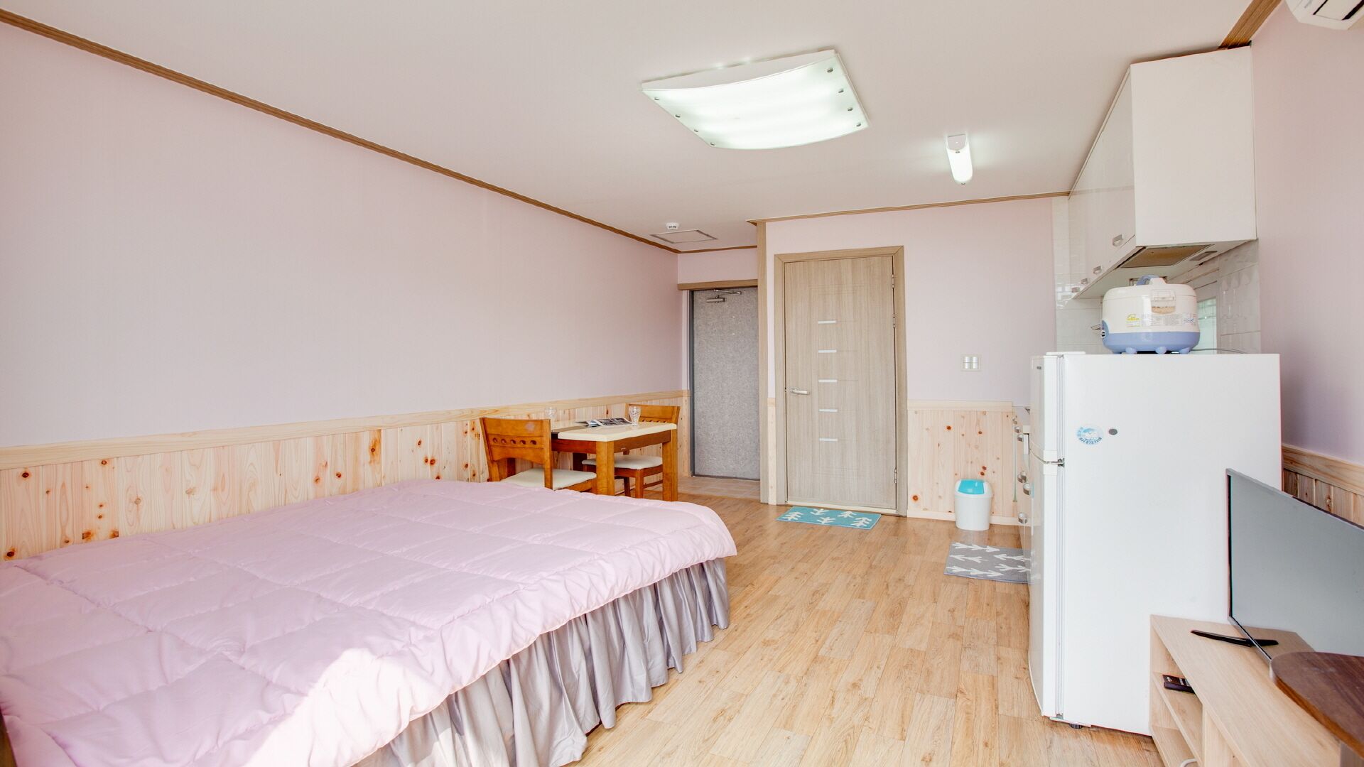 A bedroom with a bed, a desk, a chair, a wardrobe, and a refrigerator.