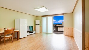 A spacious room with a wooden floor, a kitchenette with a refrigerator, a TV, and a dining area with a wooden table and chair. - Vellise Pension (Taean)