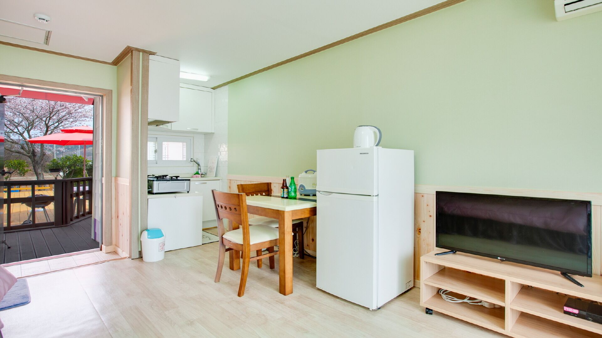 Eine kompakte Küche mit Essbereich, einem Kühlschrank und einem Fernseher auf einem Holzständer.