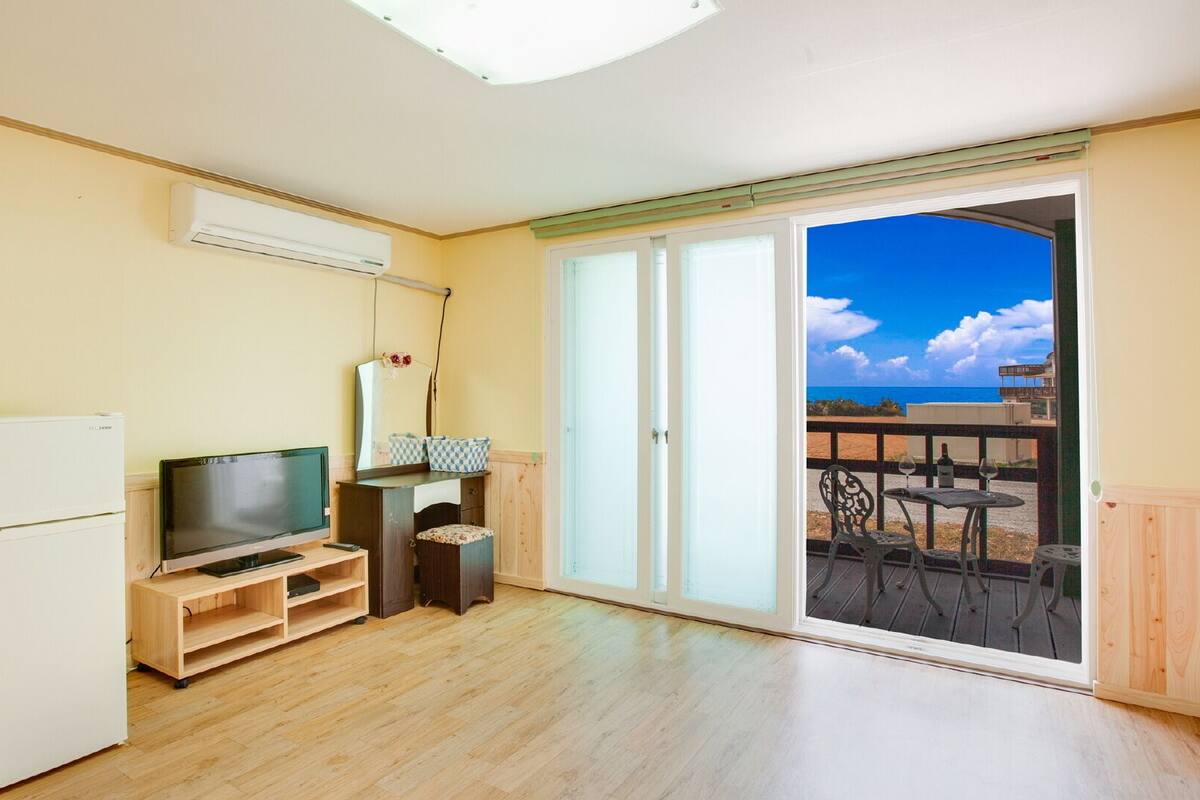 A room with a television, a small refrigerator, a wooden cabinet, and a sliding glass door leading to an outdoor area with a table and chairs.