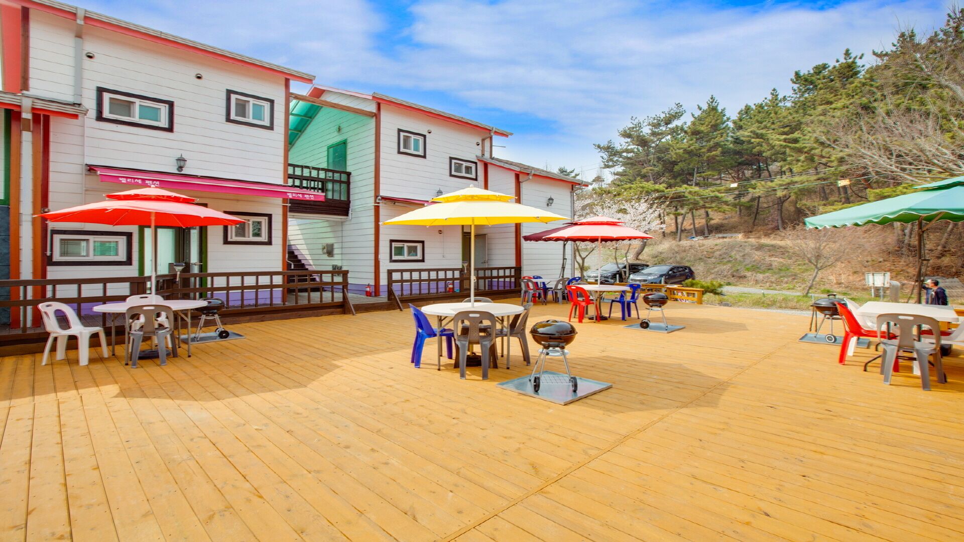 An outdoor patio with wooden flooring, tables, chairs, and umbrellas.