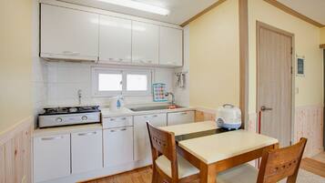 Una cocina compacta con armarios blancos, estufa a gas, lavamanos y una mesa con sillas.