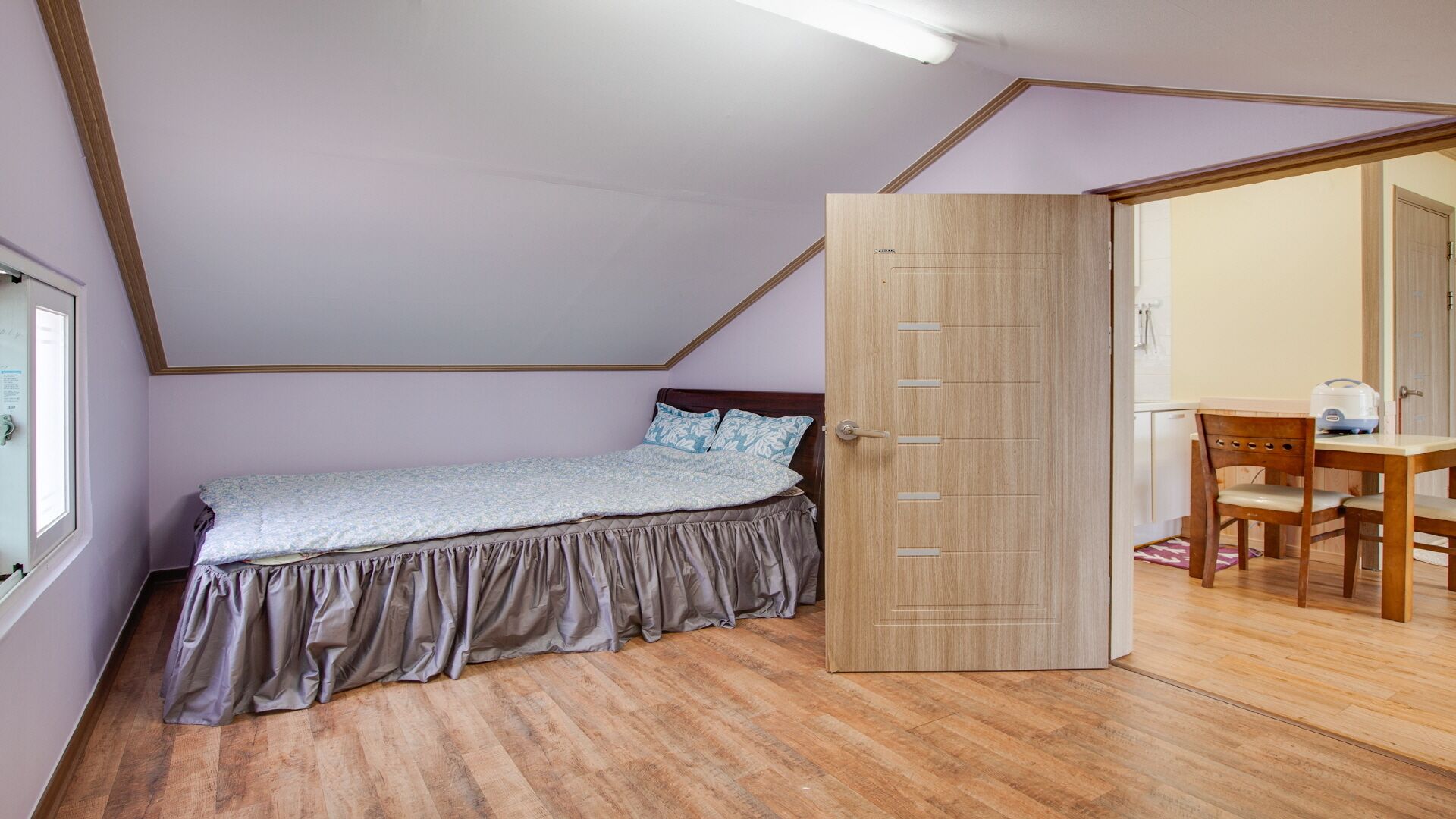 Un dormitorio con una cama, una puerta de madera y una pequeña mesa con una silla.