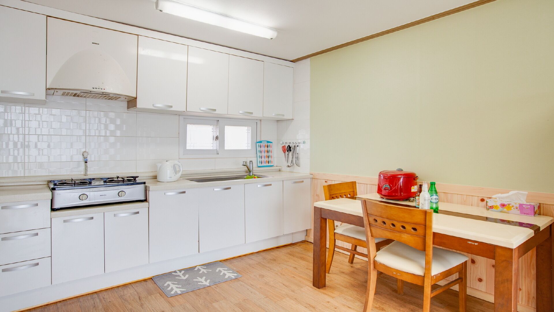 A modern kitchen with white cabinets, a gas stove, a sink, and a dining area with a wooden table and chairs.