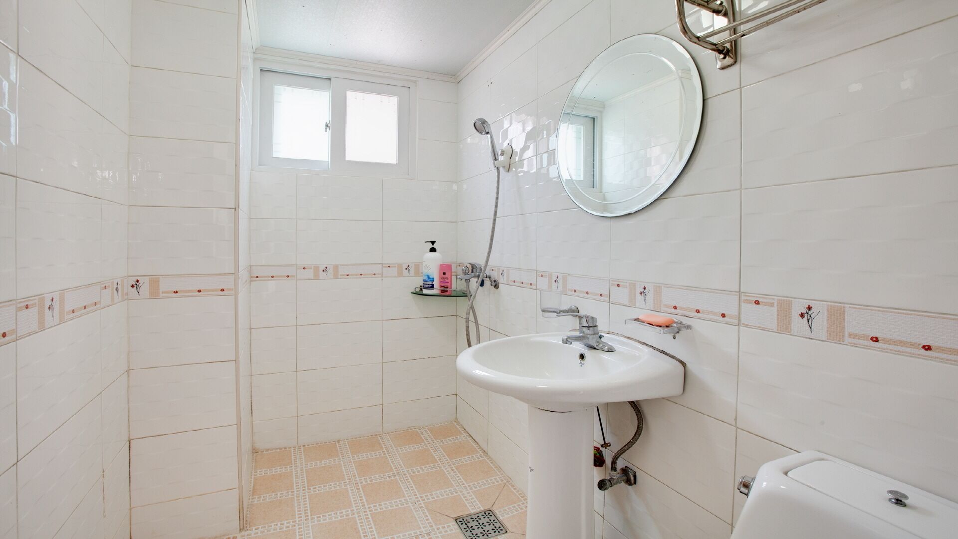 Une salle de bain avec des carreaux blancs, un lavabo, des toilettes, une douche et une fenêtre.