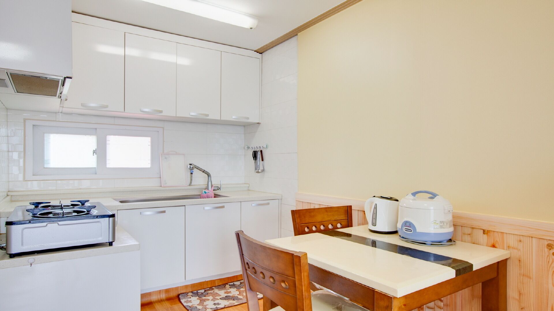A compact kitchen with white cabinets, a gas stove, a sink, and a dining area with a wooden table and chairs.