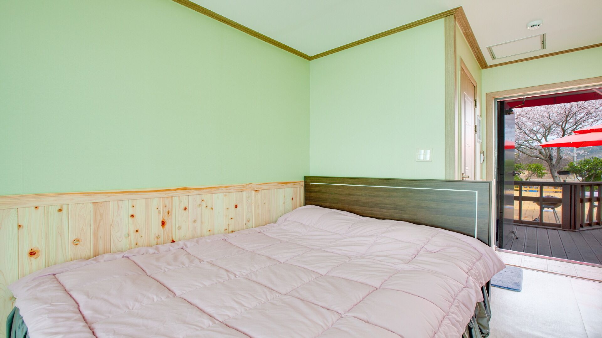 A bedroom with a bed, wooden headboard, and a view of an outdoor area with a red umbrella.